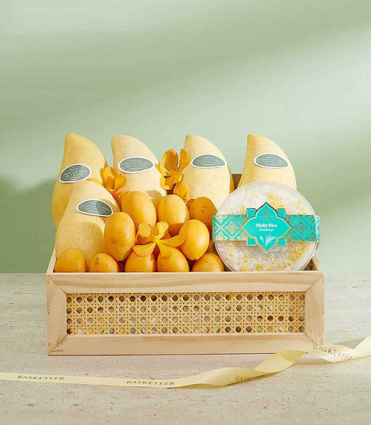 Wooden gift basket with Nam Dok Mai mangoes, golden stone fruits, yellow orchids, and sticky rice dessert