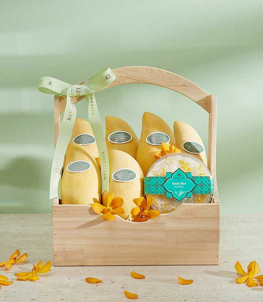 Vibrant golden Si Thong mangoes with sticky rice in wooden gift basket, tied with green ribbon and orchids