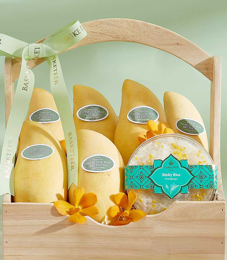 Vibrant yellow Si Thong mangoes with sticky rice and orchids in a premium wooden gift basket