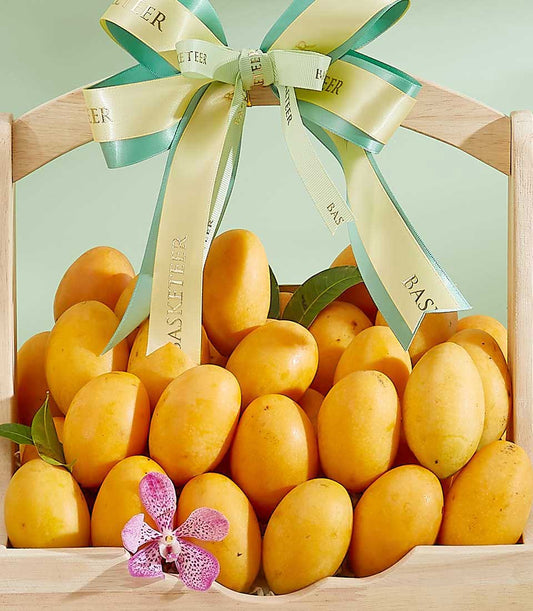 Wooden basket overflowing with golden ripe mangoes, purple orchid, and yellow-teal ribbon bow