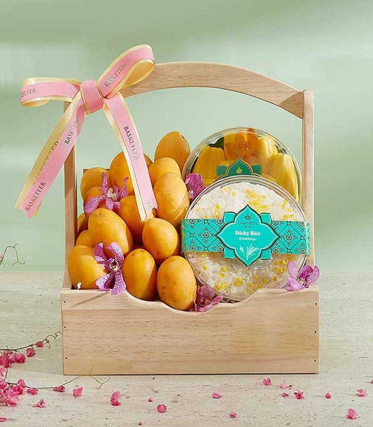 Wooden gift basket filled with fresh Thai mangoes, purple orchids, and gourmet packaged items including sticky rice and