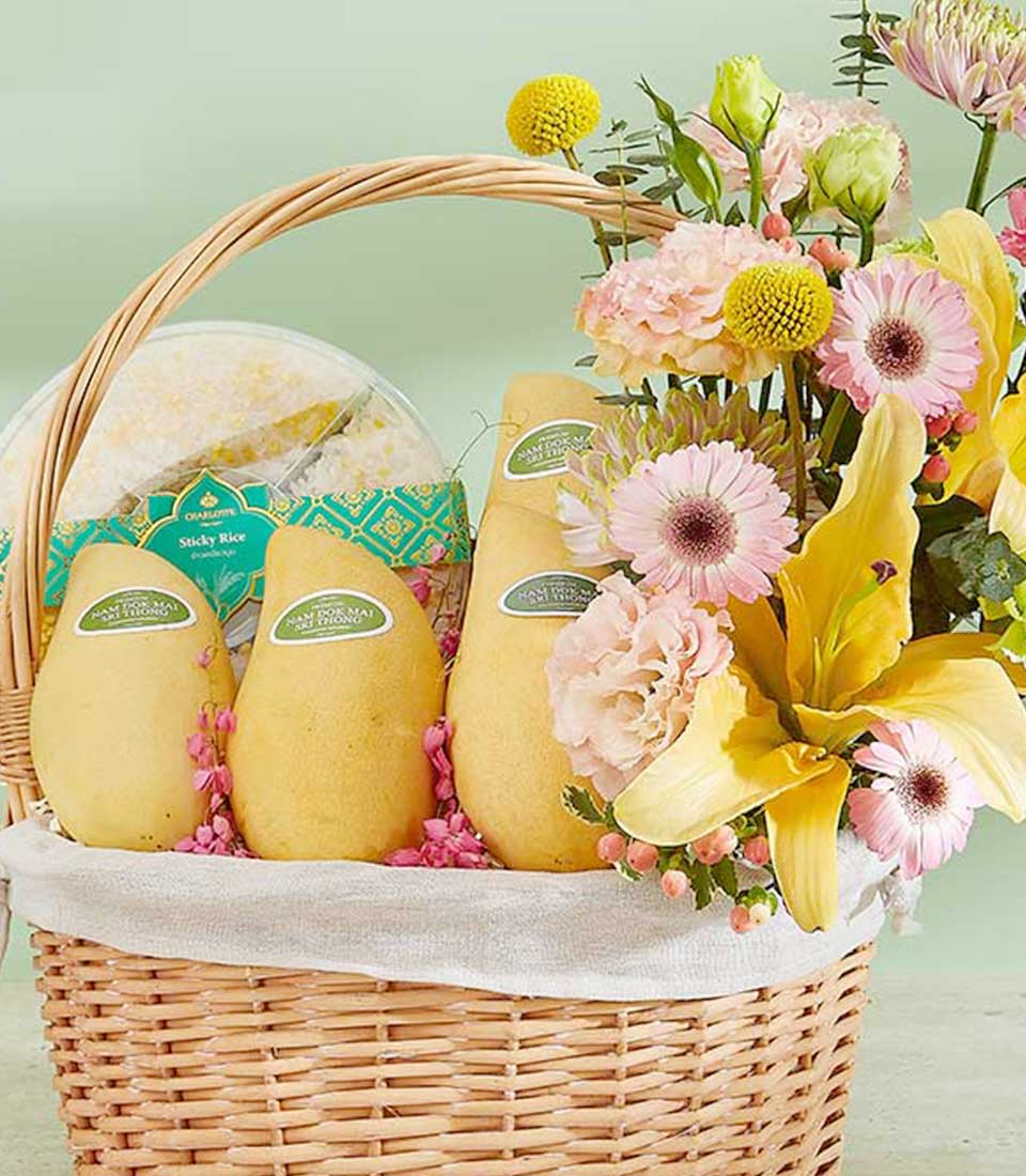 Woven wicker gift basket with ripe Thai mangoes, sticky rice, and yellow lilies with pink gerbera daisies