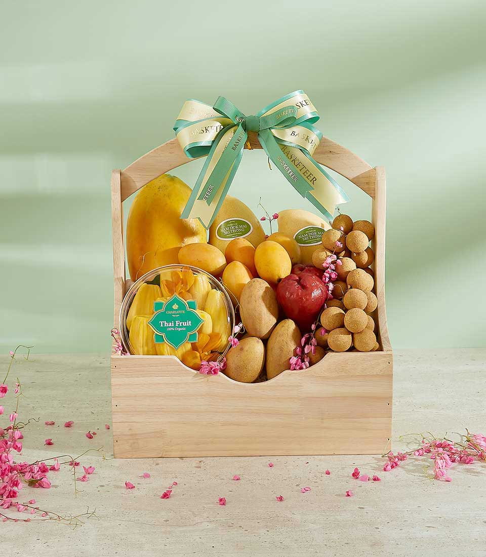 Wooden fruit basket with Thai papaya, Nam Dok Mai mangoes, longans, pomegranate, and organic jackfruit, tied with green