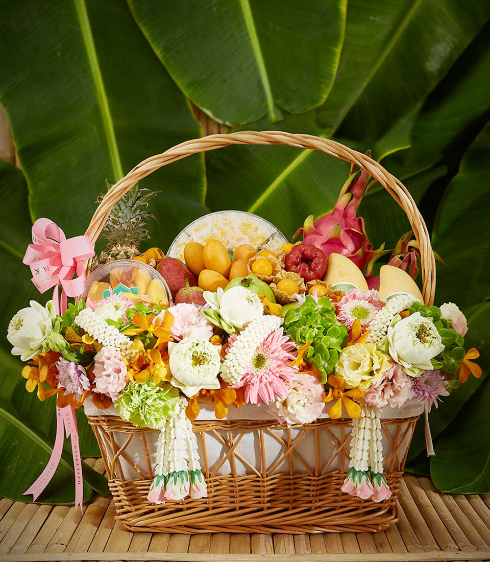 Woven wicker basket overflowing with tropical fruits, fresh flowers, and lotus blossoms for Songkran celebration