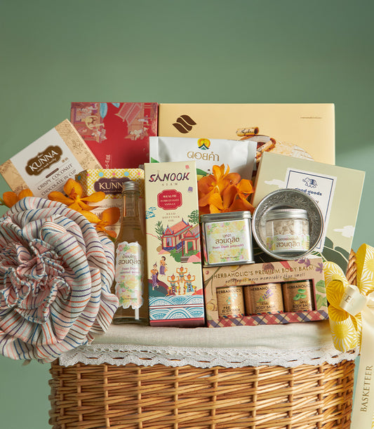Woven wicker Songkran gift basket with premium Thai wellness products, orchids, and blue-pink silk flower on light green