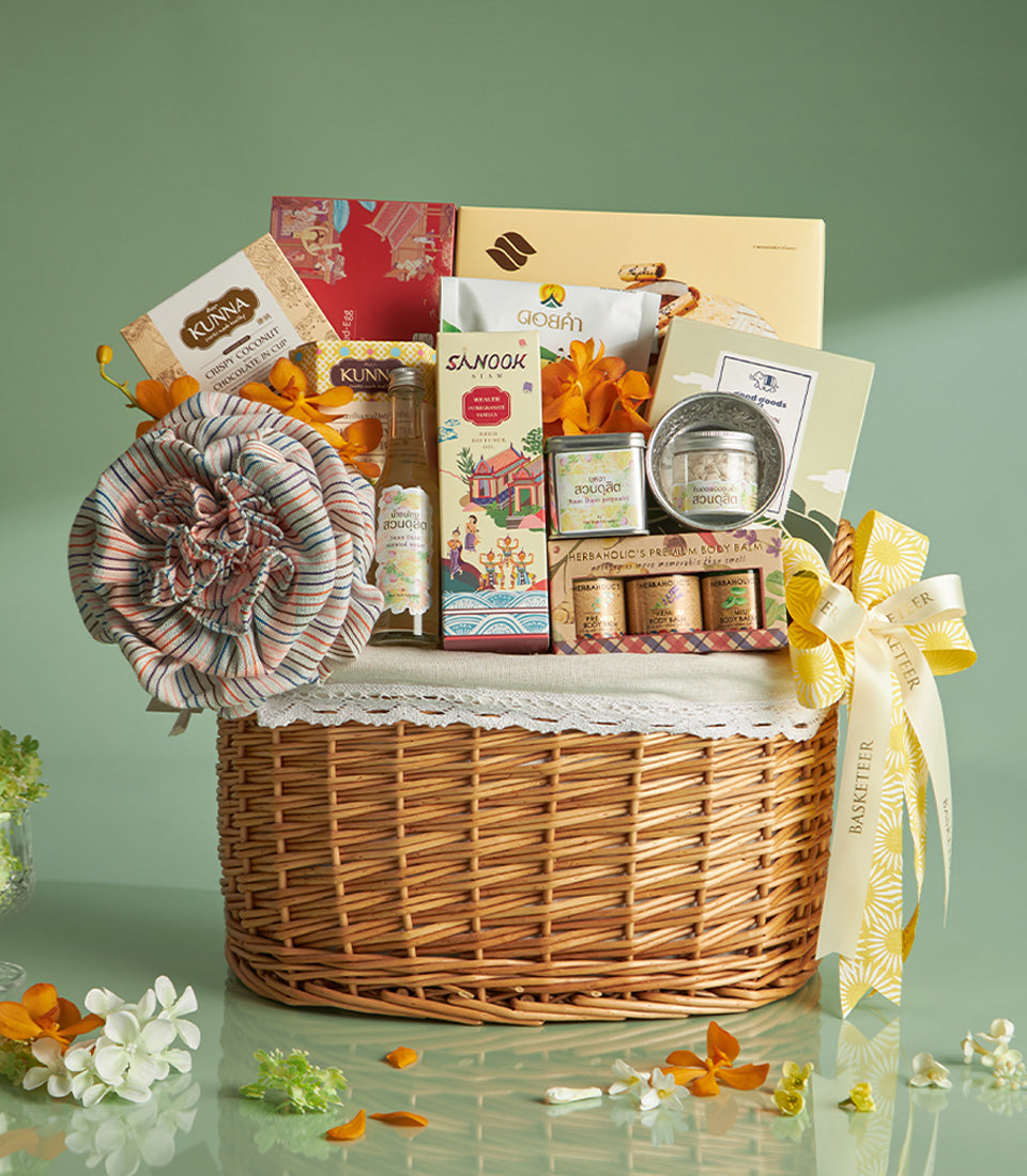 Curated wicker gift basket with artisan chocolates, body balms, and Thai gourmet treats, decorated with orange orchids for