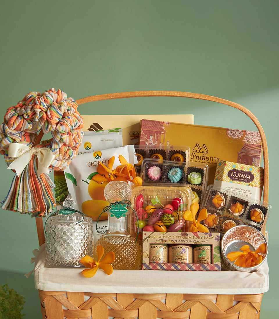 Woven gift basket with Thai New Year Songkran treats, candies, body balm, and orange orchids in warm gold tones