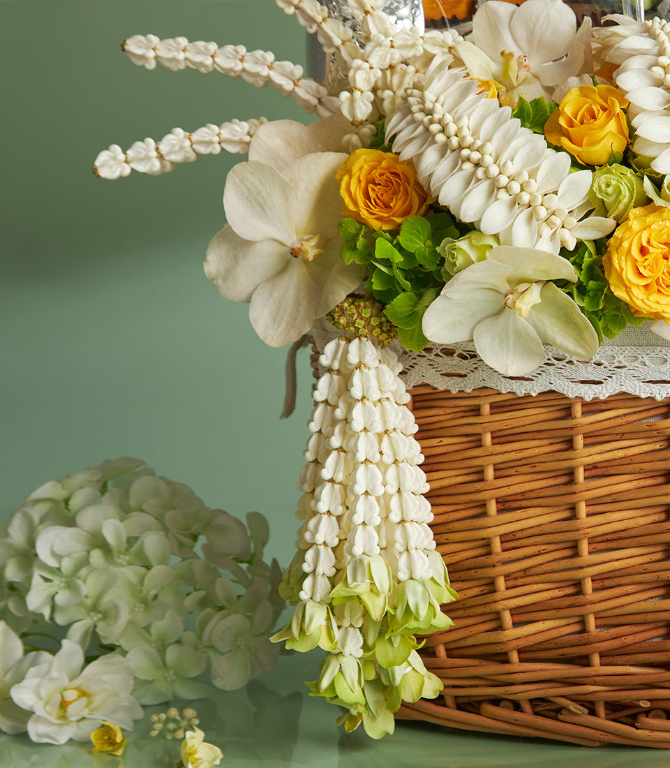 Wicker gift basket overflowing with white orchids and yellow roses, cascading white bell flower garland for Songkran Thai