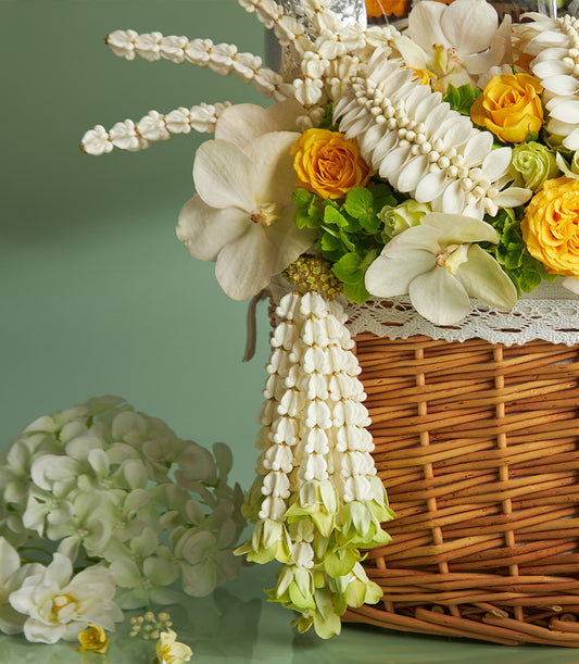 Wicker gift basket overflowing with white orchids and yellow roses, cascading white bell flower garland for Songkran Thai
