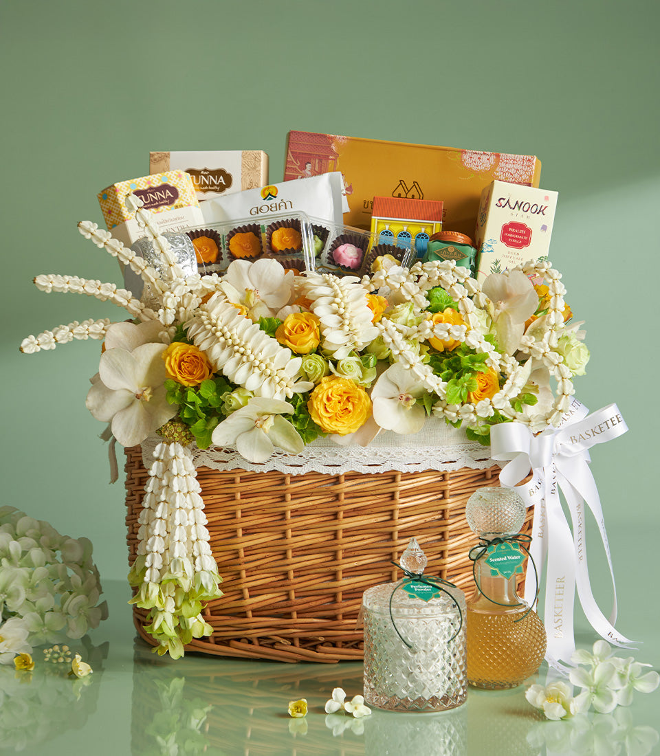 Grandeur Songkran Blessing Basket with white orchids, yellow roses, Thai garlands, gourmet sweets, and golden oils in woven