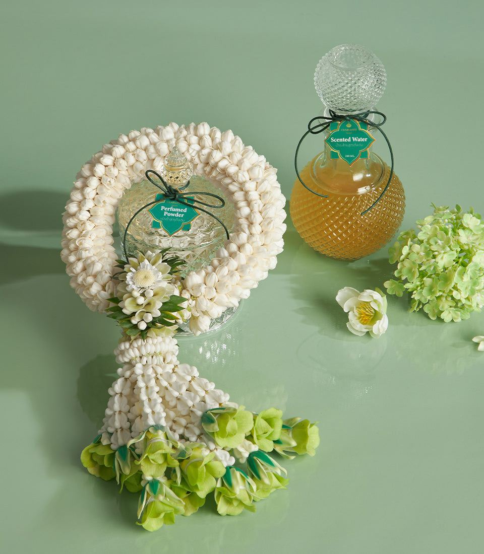 Graceful Songkran gift basket with white floral garland, perfumed powder jar, and scented water bottle on light green surface