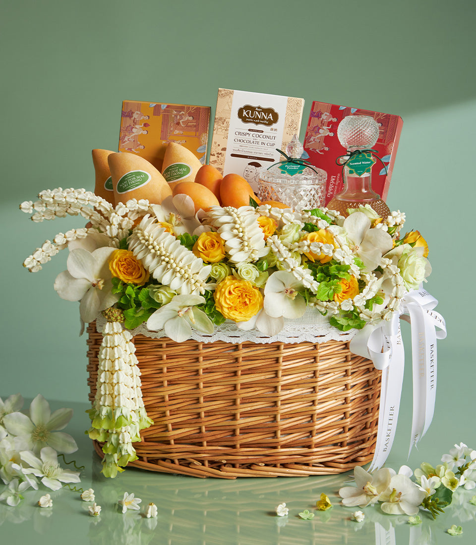 Woven wicker gift basket overflowing with white orchids, yellow roses, and Thai floral garlands, filled with mangoes,