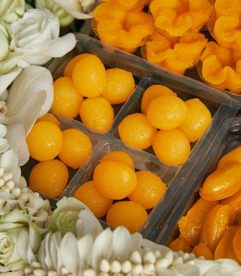 Traditional Thai auspicious desserts in golden orange, Thong Yod and Med Kanoon, with white roses and orchids for Songkran