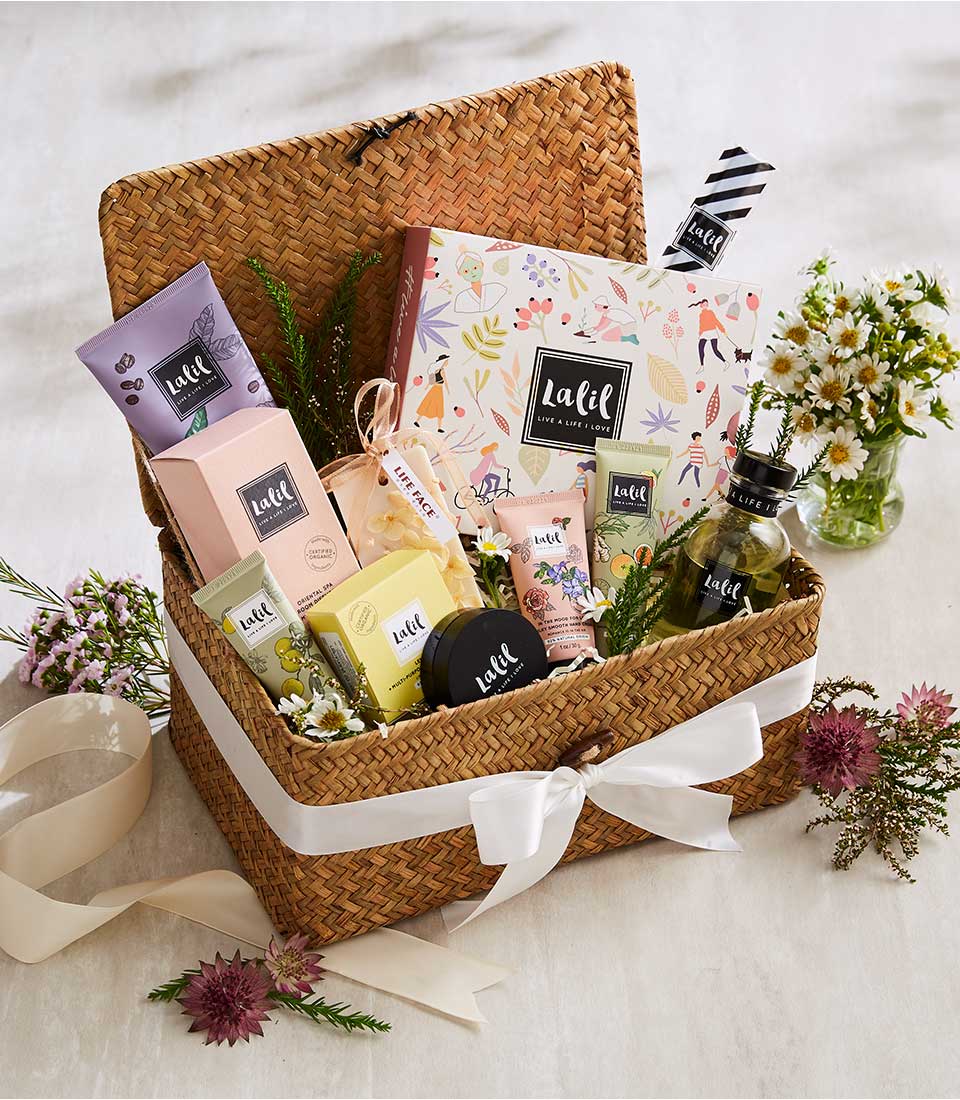 Woven spa gift basket with luxury beauty products, white satin bow, and fresh white daisies for Mother's Day