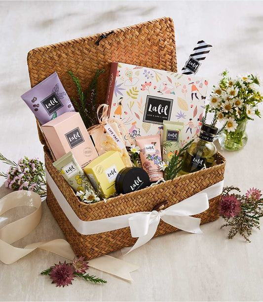 Woven spa gift basket with luxury beauty products, white satin bow, and fresh white daisies for Mother's Day