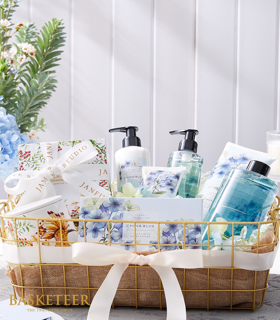 Luxe spa gift basket with gold mesh, lotion bottles, bath gel, ceramic mug, and blue hydrangea beauty collection