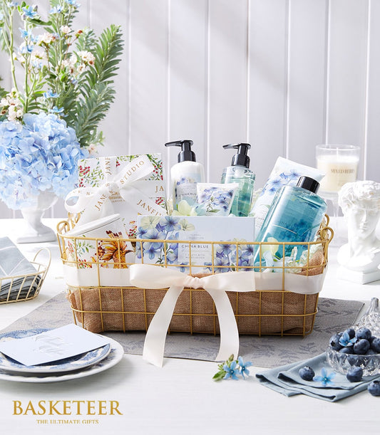 Luxury spa gift basket with blue floral bath products, gold wire design, and cream ribbon bow