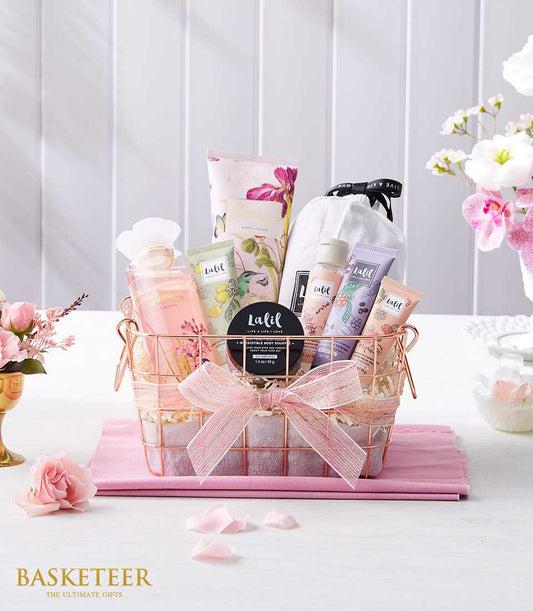 Luxury spa gift basket with rose gold wire design, pink ribbon bow, bath and body products, and fresh pink roses