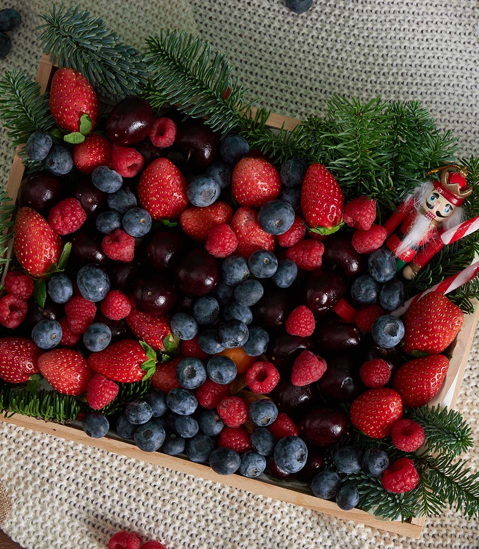Festive mixed berry gift box with strawberries, blueberries, raspberries, and cherries on cream knit blanket
