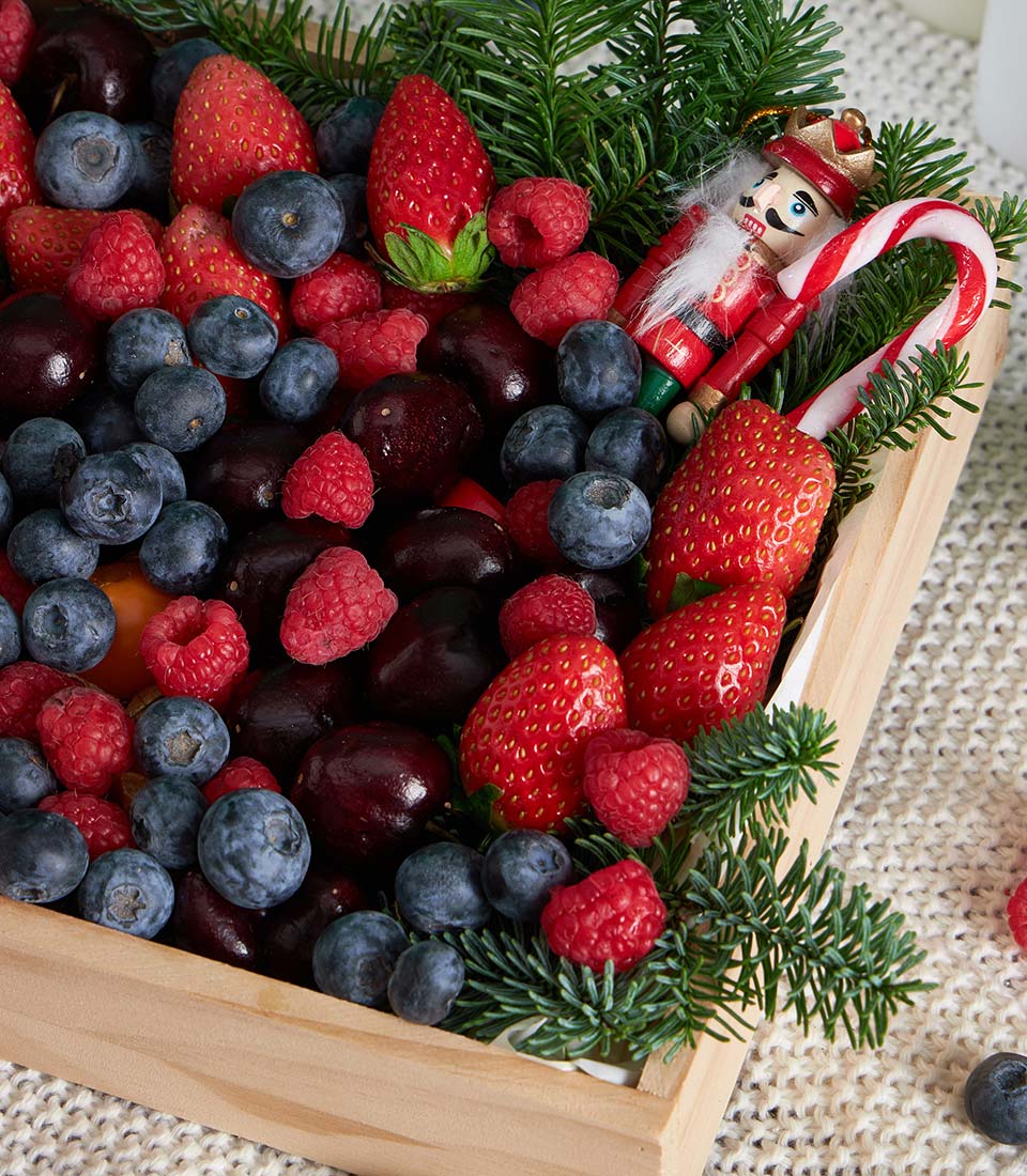 Festive mixed berry wooden box with strawberries, blueberries, raspberries, pine sprigs, and holiday ornaments