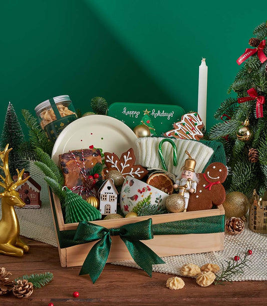 Festive wooden gift box with fruitcake, gingerbread cookies, ceramic plate, mug, nutcracker, and scarf for Christmas