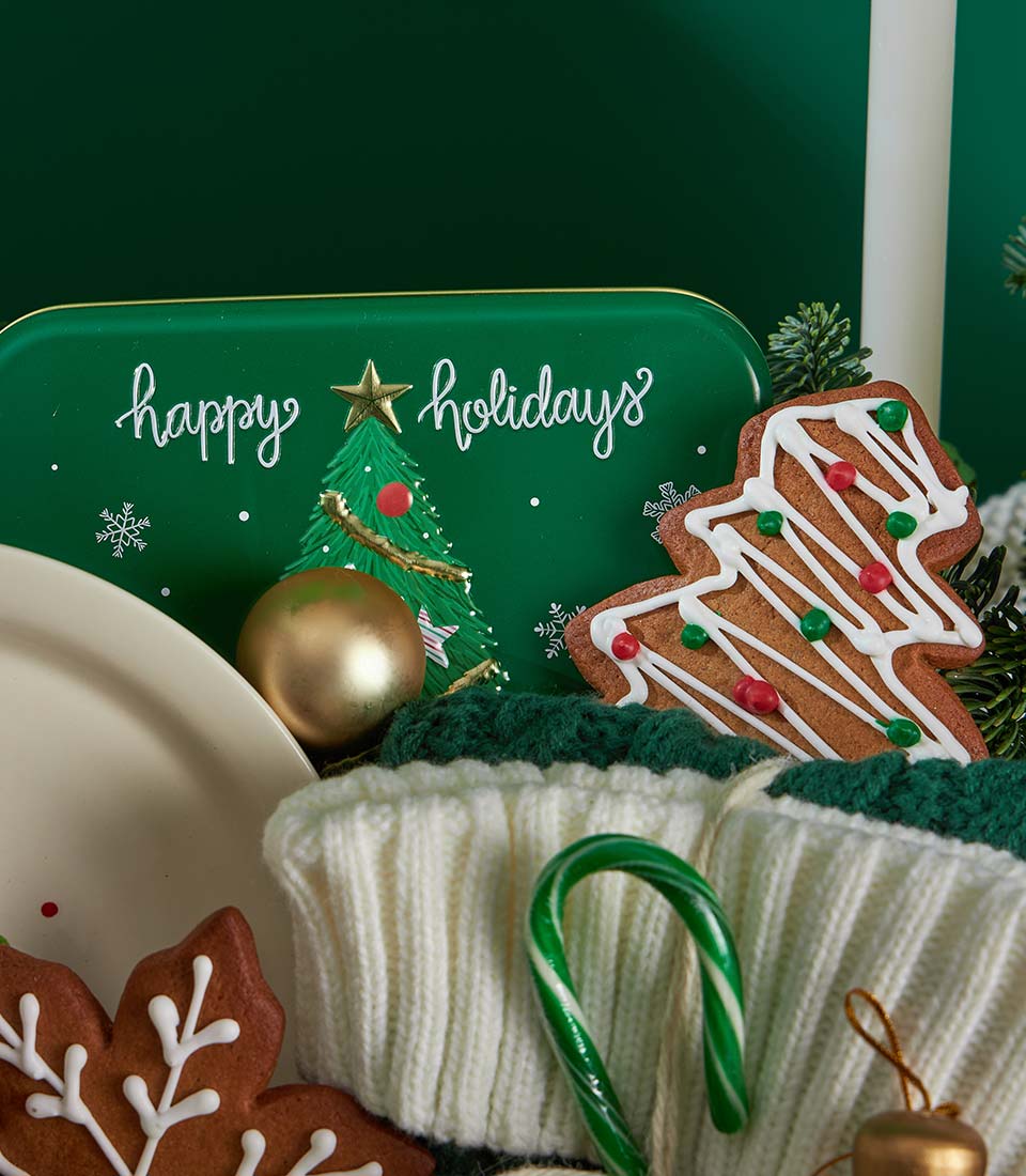 Festive Christmas cookies and fruitcake gift basket with gingerbread, candy cane, and holiday tin on dark green background