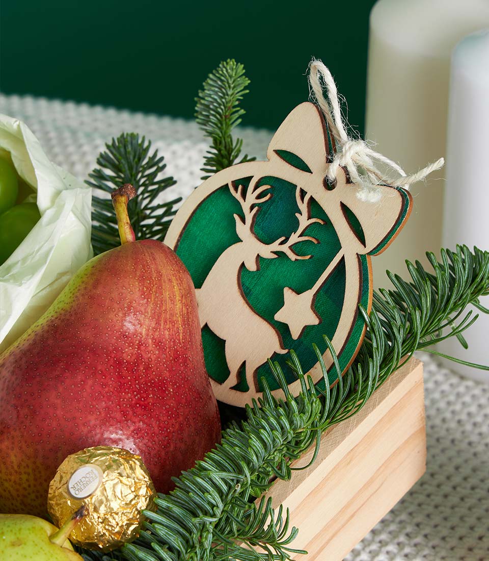 Festive wooden crate with fresh pear, Ferrero Rocher chocolate, and grapes topped with reindeer ornament and pine sprigs