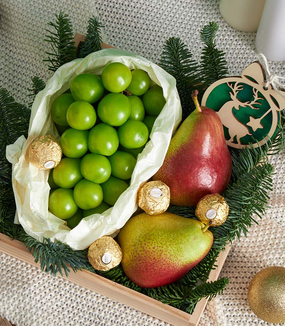Festive wooden gift tray with green fruit, Ferrero Rocher chocolates, pine branches and Christmas ornaments