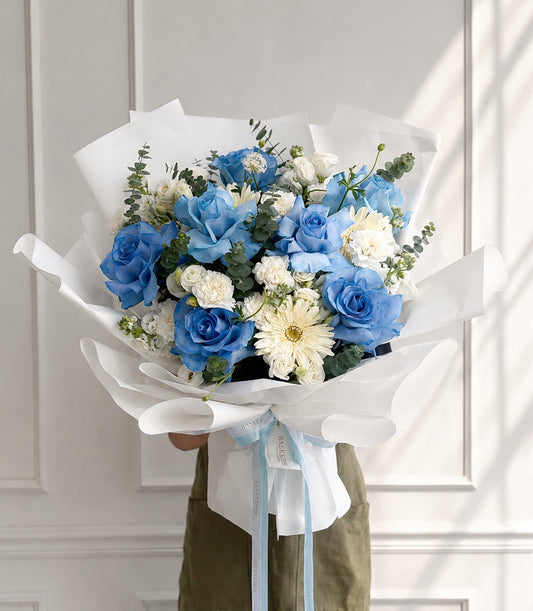 An elegant Flowers by Basketeer bouquet featuring vibrant blue roses, delicate white spray carn