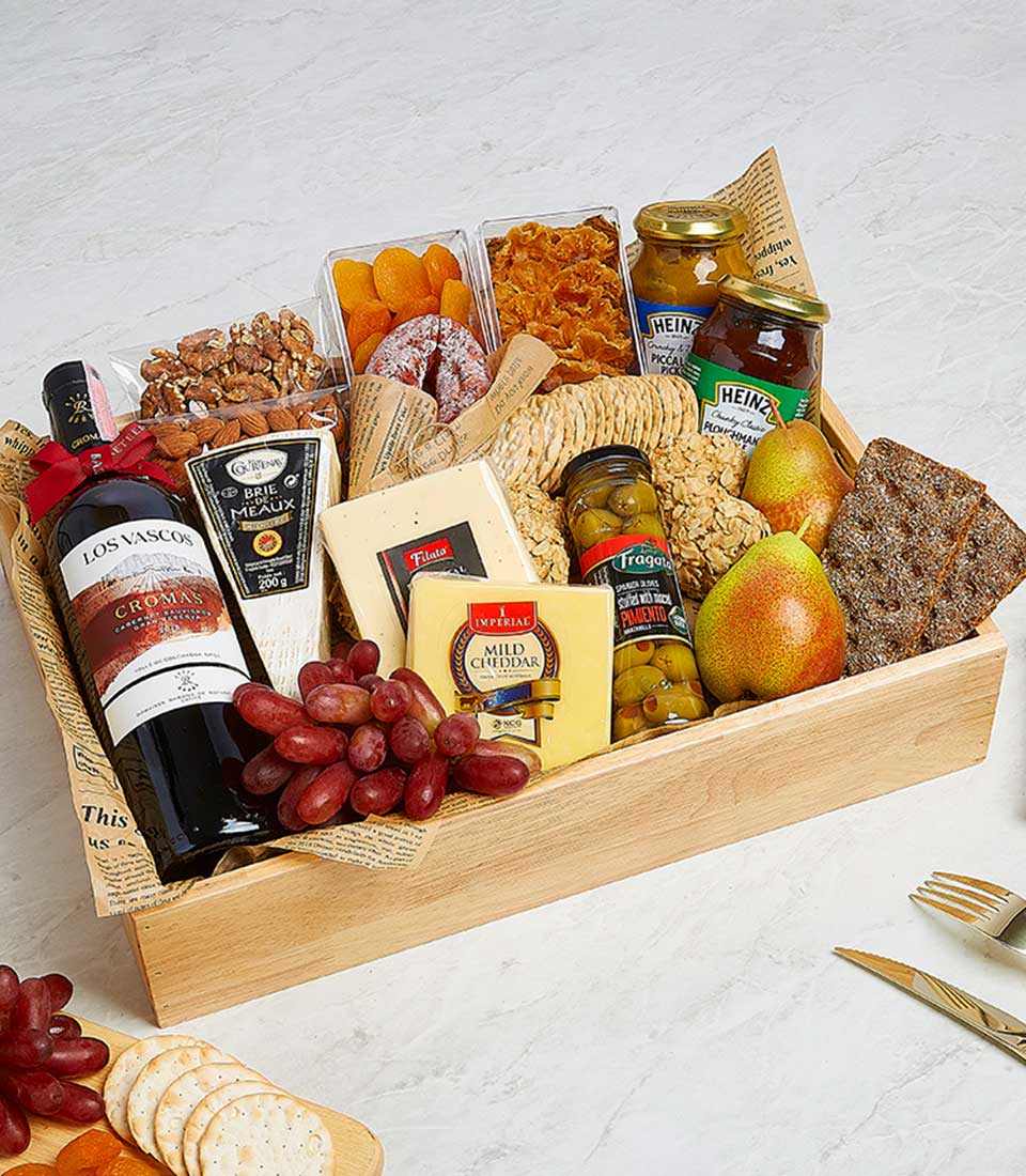Premium red wine and gourmet cheese hamper in wooden tray with Brie, cheddar, grapes, crackers, and artisan preserves