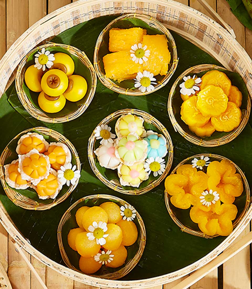 Assorted Thai desserts in woven baskets on banana leaf, Songkran gift set with golden sweets and white flowers