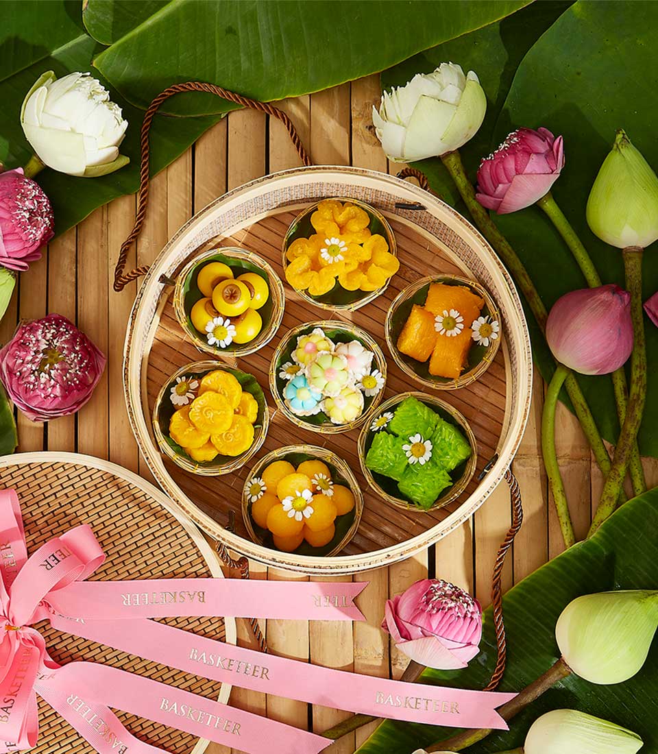 Artisan Thai desserts in bamboo cups on woven tray with lotus flowers and banana leaves for Songkran