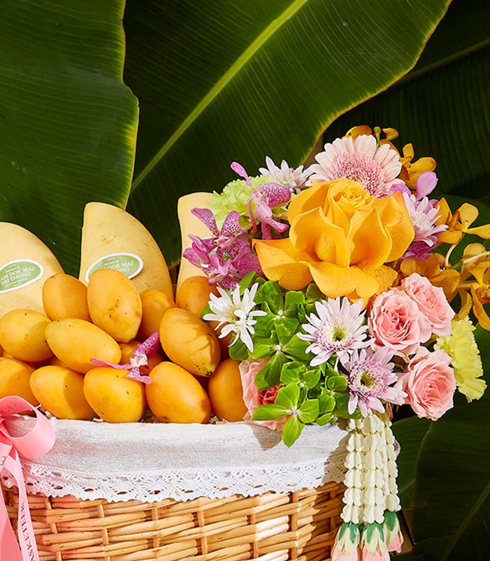 Woven gift basket with fresh yellow mangoes and vibrant tropical flowers including roses, orchids, and daisies with Thai