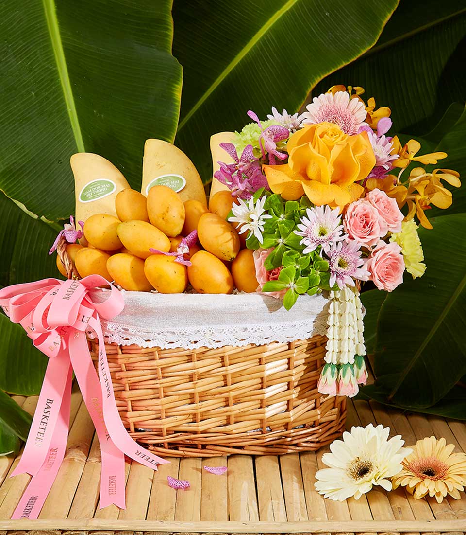Woven wicker gift basket with fresh yellow mangoes and vibrant mixed flower bouquet, tropical Songkran celebration hamper