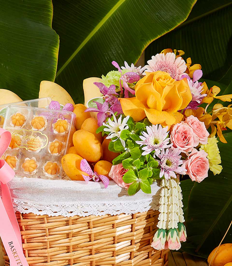 Tropical Songkran celebration basket with yellow mangoes, flower-shaped desserts, and vibrant roses, orchids, daisies with