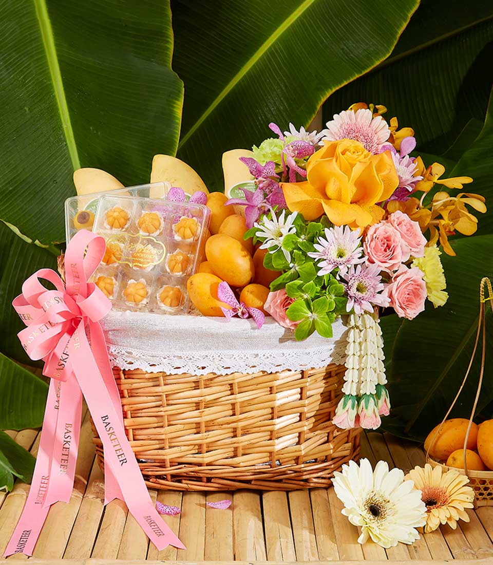 Tropical Songkran wicker hamper with fresh mangoes, flower-shaped desserts, and mixed roses and gerbera daisies with pink
