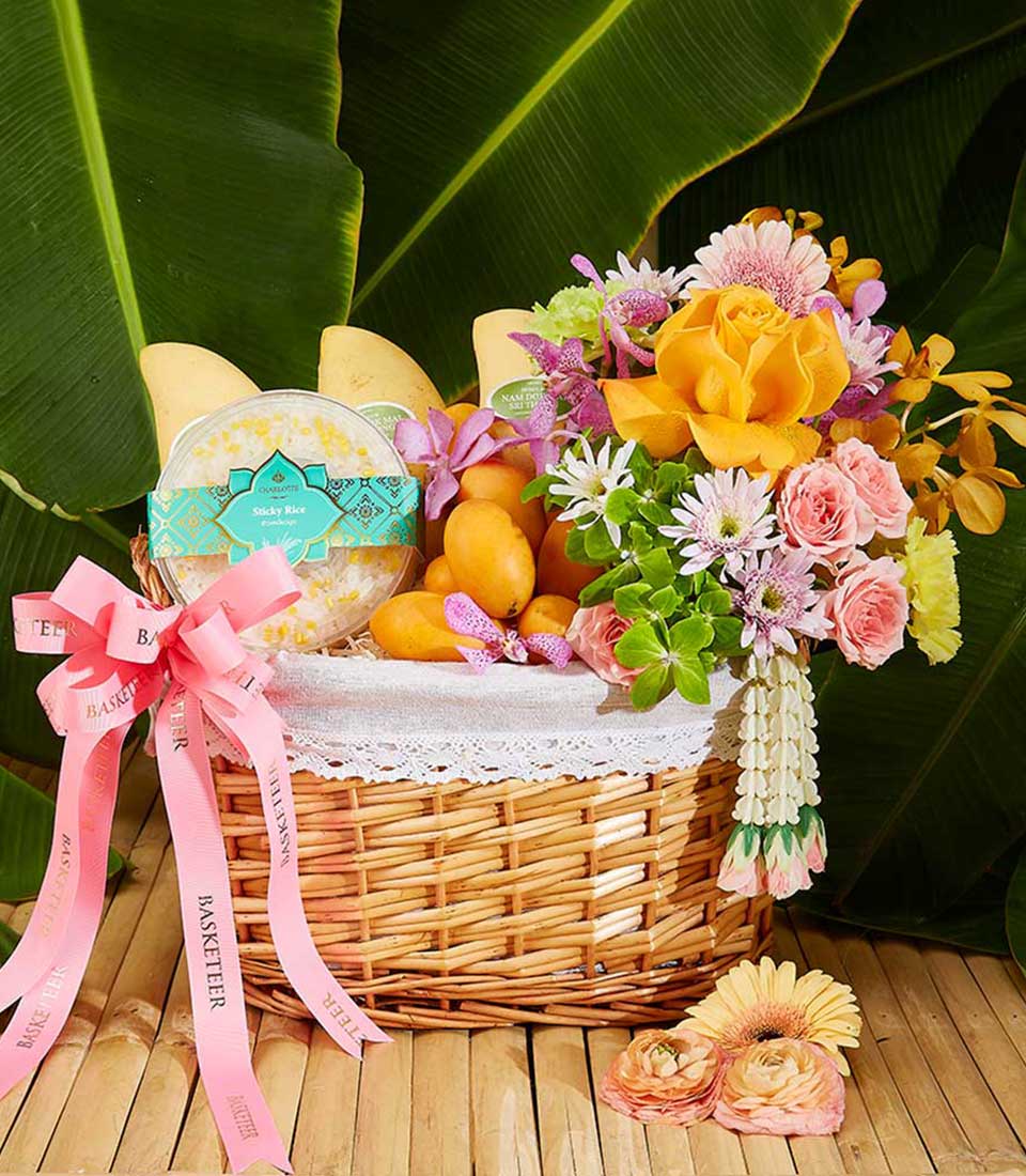 Vibrant Thai New Year gift hamper with tropical mangoes, sticky rice, and mixed flower bouquet in wicker basket