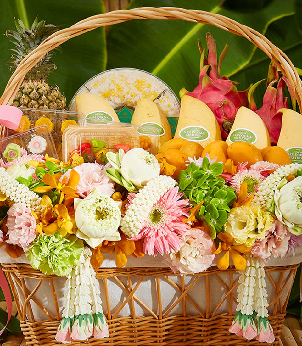 Wicker gift basket overflowing with Nam Dok Mai mangoes, dragon fruit, pineapple, Thai desserts, and fresh lotus, gerbera,