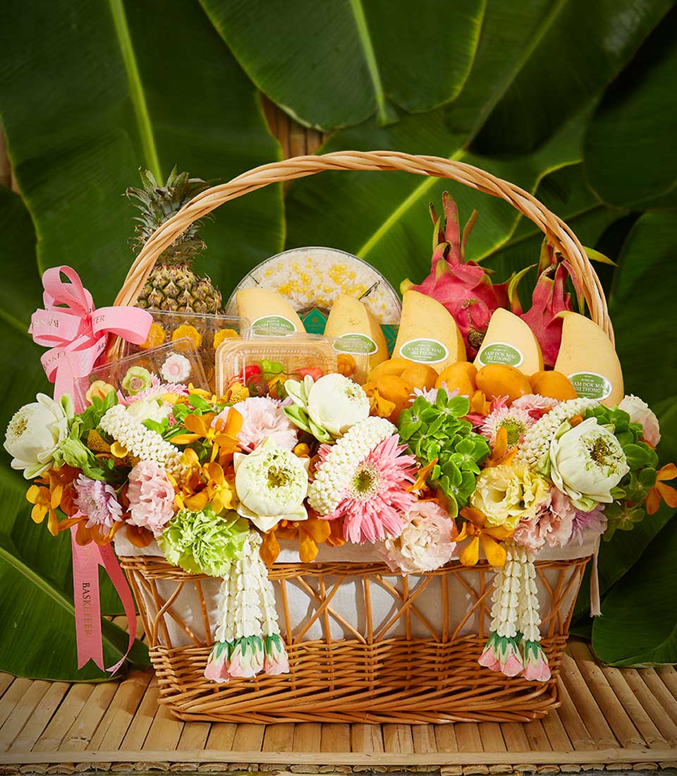 Woven wicker gift basket with Thai fruits, sticky rice, and fresh white, pink, and yellow flowers for Songkran celebration