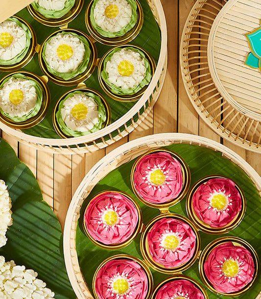 Elegant Thai New Year gift set with lotus-shaped desserts in gold cups on woven bamboo trays with banana leaves