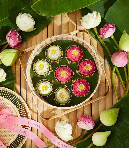 Lotus-themed Thai sweet gift set with golden dessert cups on bamboo tray, fresh pink and white lotus flowers for Songkran