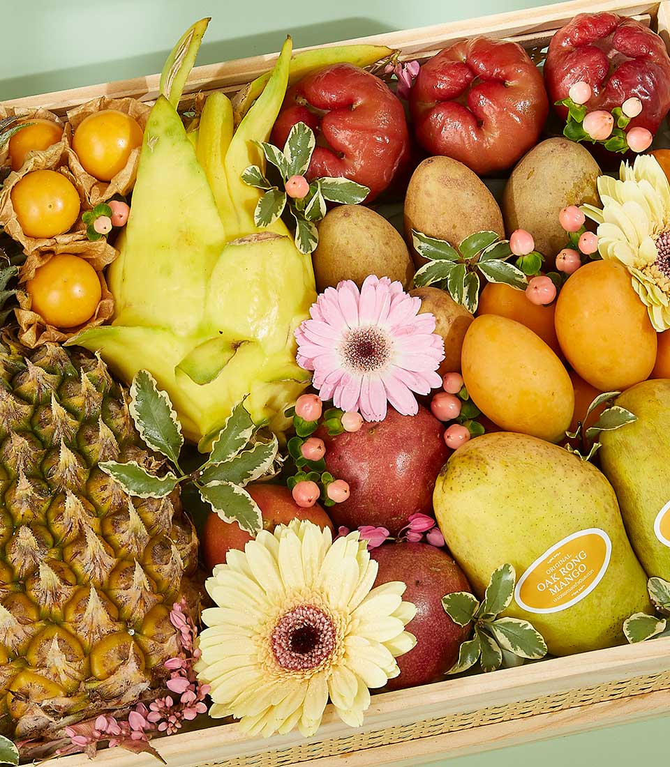 Vibrant tropical fruit gift basket with dragon fruit, pineapple, mangoes, rose apples, and pink gerberas in wooden crate