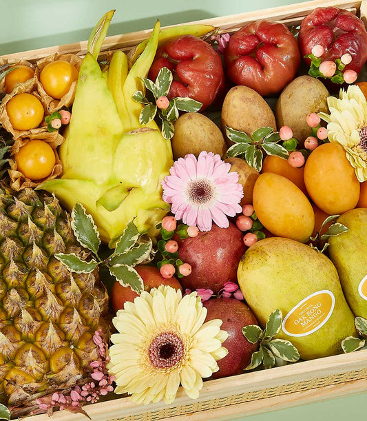 Vibrant tropical fruit gift basket with dragon fruit, pineapple, mangoes, rose apples, and pink gerberas in wooden crate