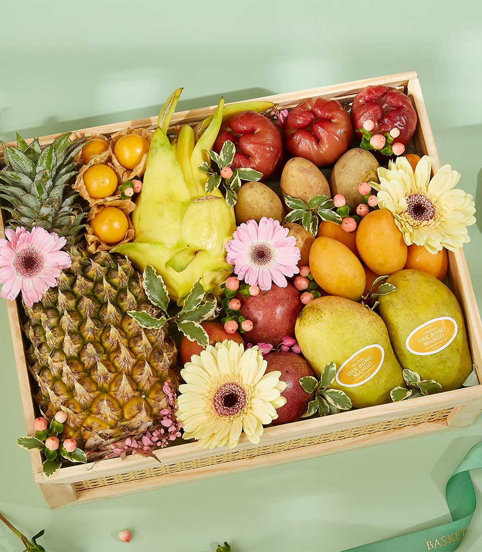 Wooden basket filled with fresh Thai tropical fruits, pineapple, mangoes, and star fruit, decorated with pink gerbera daisies