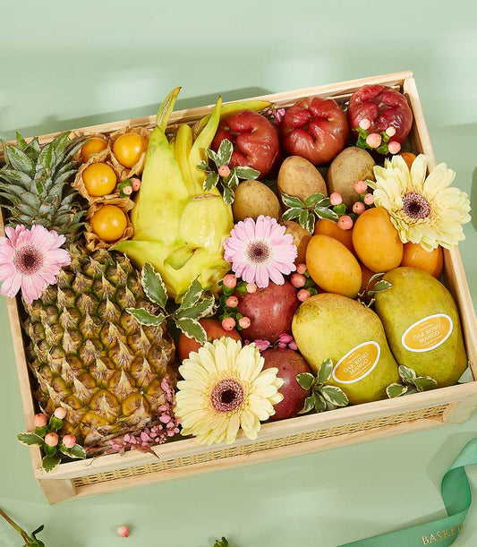 Wooden basket filled with fresh Thai tropical fruits, pineapple, mangoes, and star fruit, decorated with pink gerbera daisies