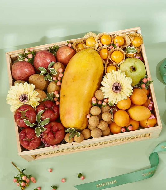 Wooden gift box with tropical fruits including papaya, apples, kumquats, longan, and fresh gerbera daisies