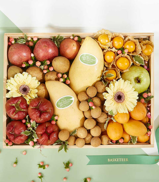 Tropical Harvest wooden gift box with premium Nam Doc Mai mangoes, pomegranates, longans, and fresh flowers