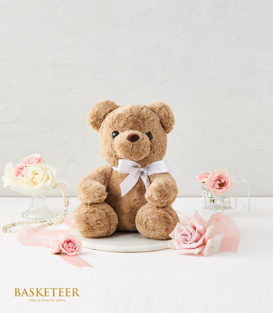 Brown plush teddy bear with white ribbon, paired with fresh roses and romantic gift styling