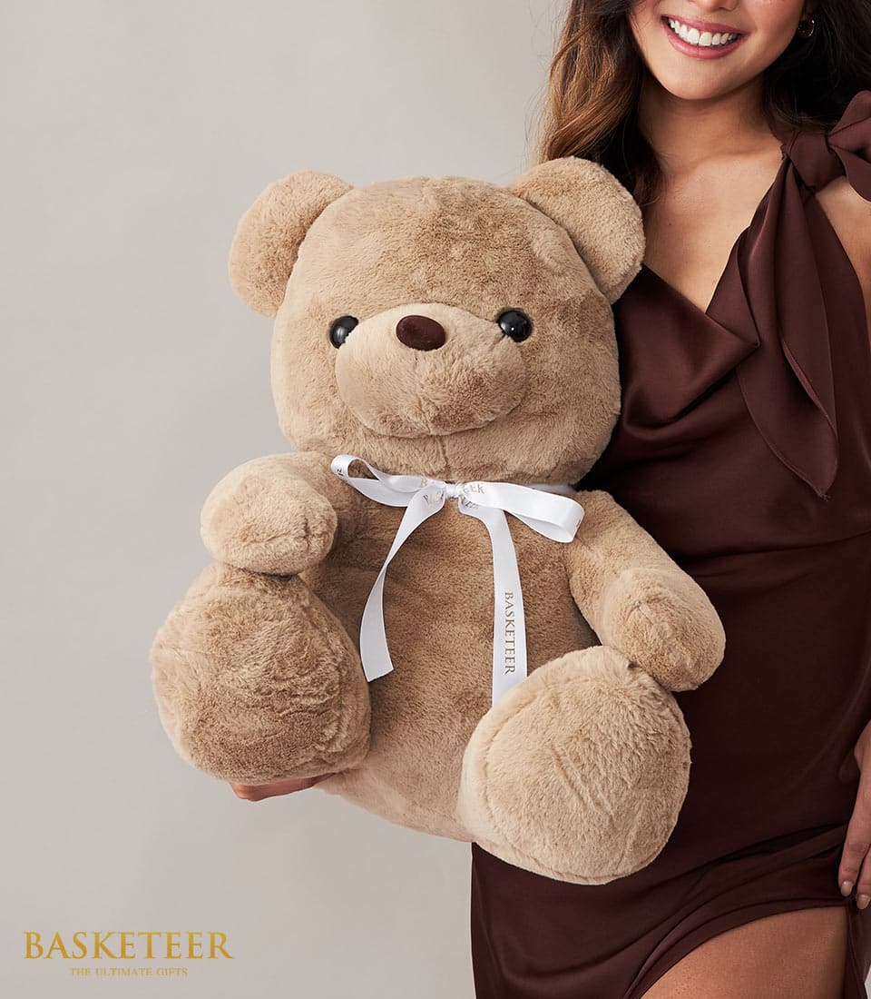 Large light brown plush teddy bear with satin ribbon bow for gifting