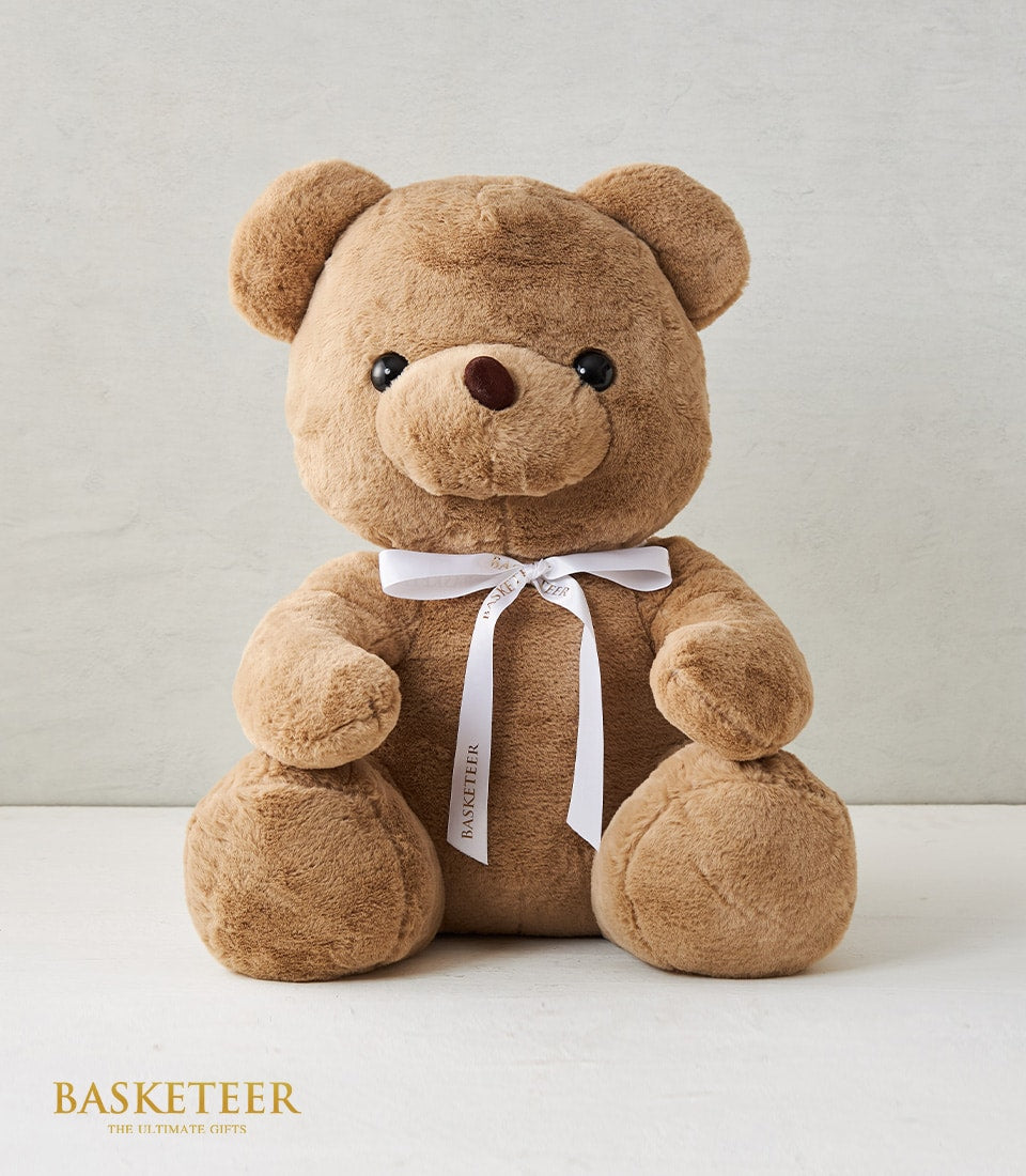 Soft plush teddy bear in light brown with white satin ribbon bow and Basketeer branding